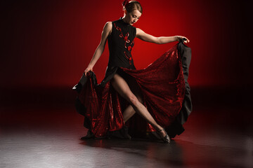 young and beautiful woman touching dress while dancing flamenco on red