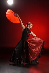 elegant flamenco dancer touching dress and holding fan while dancing on red
