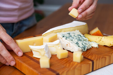 Obraz na płótnie Canvas Woman taking piece of cheese from wooden board. Blue, soft and hard cheeses. Studio shot. Selective focus. Side view. Dairy meal and cooking on isolation concept for flyers and banners