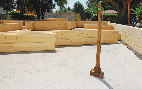 An Old Wooden Sledge Hammer On The Foundations Of A Partially Constructed Wood (fir) Block House, A Pre-cut Wooden House Which Is Assembled On-site
