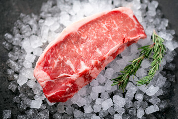 Raw fresh New York beef steak on ice with herbs and rosemary, close up