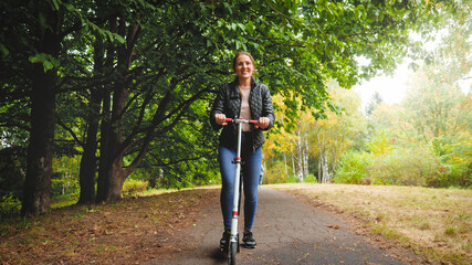 Beautiful smiling young woman riding on kick scooter at autumn park © Kyrylo Ryzhov