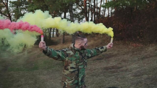 Soldier in a camouflage uniform plays with pink and yellow smoke