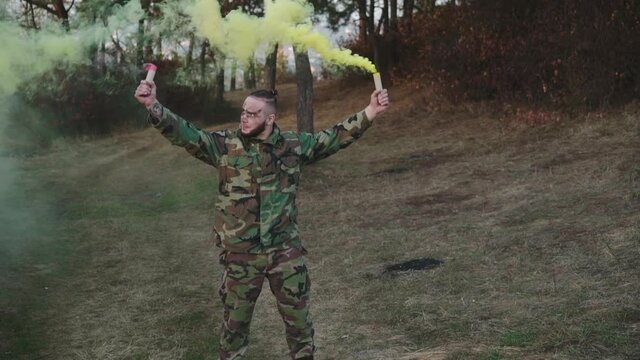 Soldier in a camouflage uniform and walks in nature with colored smoke