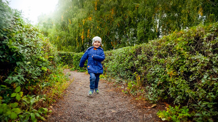 Obraz premium Happy laughing little boy in jacket running in bush labyrinth at autumn park