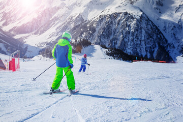 Fototapeta na wymiar Two kids 10 years old racing down the slope on sunny day in Alpes mountains, view from behind