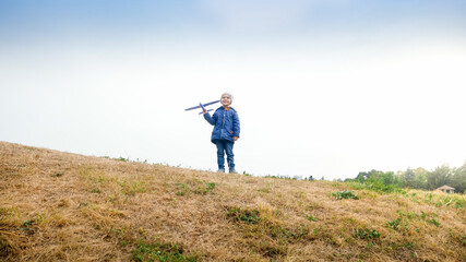 Happy smiling little boy standing on hill top with toy airplane