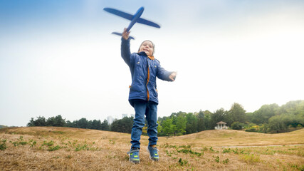 Portrait of happy excited little boy launching and throwing toy airplane in the field