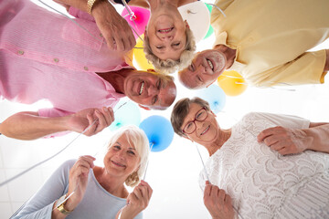 Low angle of happy senior friends in the circle with balloons during birthday party