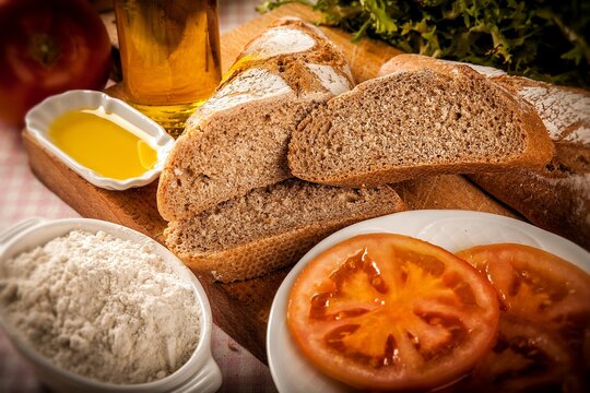 rebanadas de pan de espelta con decoraci&oacute;n de tomate y aceite de oliva sobre madera