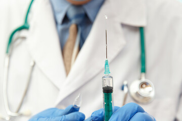 Doctor in mask holding a medical injection syringe and stethoscope.