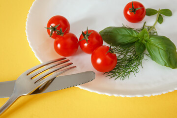 Chery tomatoes on a plate with basil and cutlery.