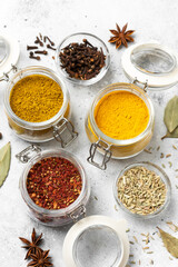 Spices and condiments in glass jars on a light gray table. Spices: turmeric, curry, star anise, fennel and cloves close-up with space for text