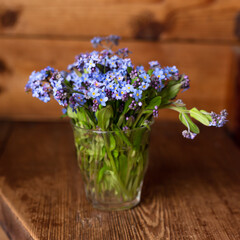 Forget-me-nots in a vase on a wooden background.