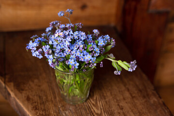 Blue wildflowers in a glass cup on a wooden background. Forget me nots.