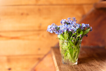 Blue wildflowers in a glass cup on a wooden background. Forget me nots.
