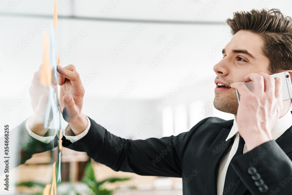 Wall mural Image of concentrated businessman talking on cellphone while working