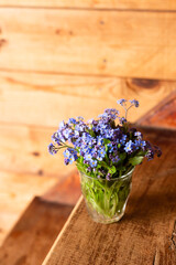 Blue wildflowers in a glass cup on a wooden background. Forget me nots.