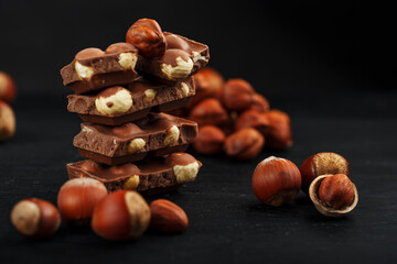 Chocolate with hazelnuts in the form of a tower on a dark background, surrounded by nuts in the...