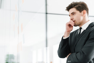 Image of thinking young businessman using stickers while working