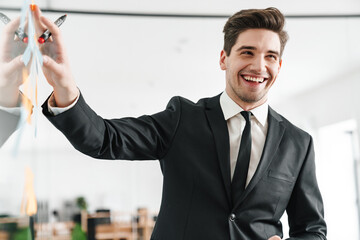 Image of concentrated young businessman wearing suit using stickers while working in office