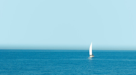 Boat with sail sailing in Spain sea with clear sky at sunrise