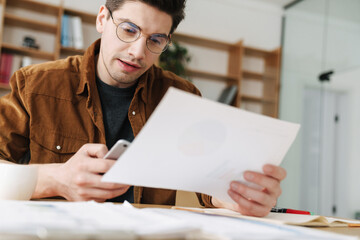 Image of handsome man using mobile phone while working with documents