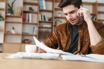Image of handsome man talking cellphone while working with documents