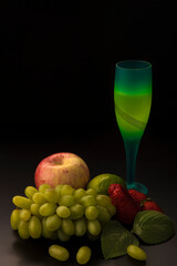 Still life on a black background. Apple, grape, strawberry, lime and glass
