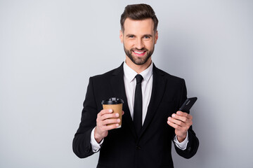 Portrait of positive charming trader man hold take-away americano hot beverage mug use his smartphone always connection concept wear black jacket isolated grey color background