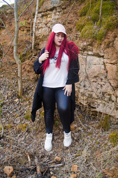 A chubby girl in a jacket and jeans with red hair against a stone wall