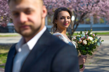 Groom in defocus blues in the foreground, in the background in focus is weightless with flowers. bride, against the background of pink spring floral Sakura, newlyweds, spraying with rose petals.