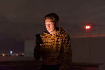 Young handsome man using phone at rooftop of the building during stormy weather at night