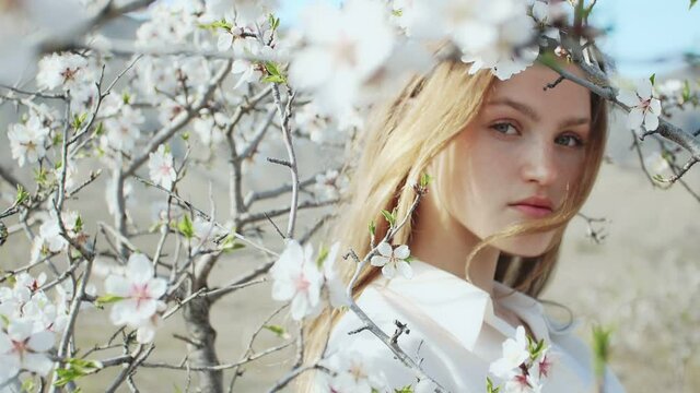 beautiful young woman in the spring rays of the sun among the flowering branches of the mine tree slow motion