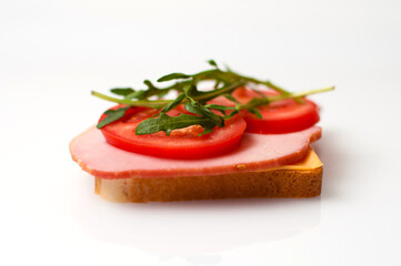 Fototapeta na wymiar Sandwich made of balyk, cheese, bread, tomatoes and arugula on a white plate side view