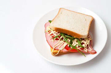 Tasty sandwich with ham or balyk, tomato, arugula, cheese, mayonnaise and white bread for toast on a plate on a white background view from the top flat lay, copy space