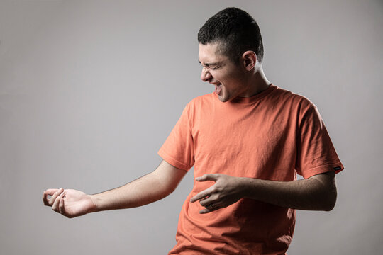 Ragazzo giovane con t-shirt arancione simula il gesto del suonare la chitarra con le mani, isolato su sfondo grigio