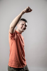Ragazzo giovane con t-shirt arancione fa un gesto di esultanza , isolato su sfondo grigio © alex.pin