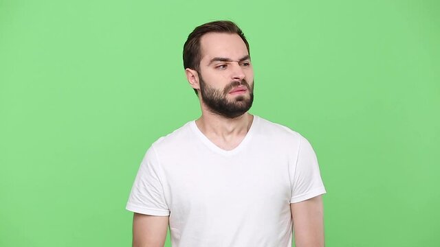 Young sad fun displeased disgusted abhorred bearded guy 20s in white t-shirt isolated on green chroma key background studio. People emotions lifestyle concept. Close cover nose with hand sniff smell