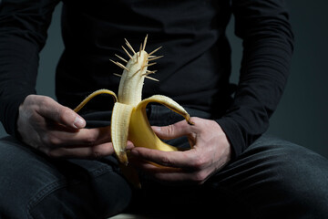 sexually transmitted diseases concept. A man in black with a prickly banana in his hand, on a gray...