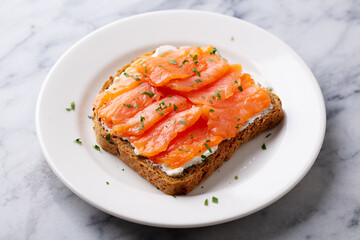 Sandwich, toast with smoked salmon and cream cheese on white plate. Marble background. Close up.