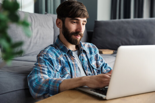 Image of pleased man working with notebook while sitting on floor