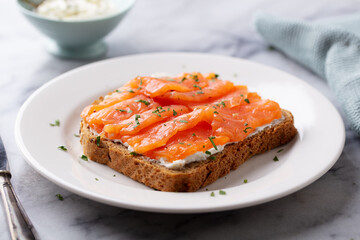 Sandwich, toast with smoked salmon and cream cheese on white plate. Marble background. Close up.