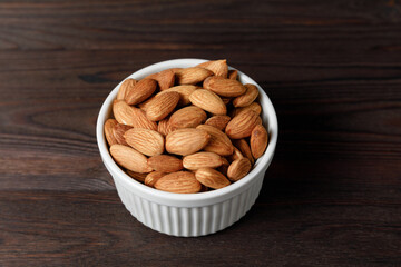 Almonds in white porcelain bowl on wooden table.