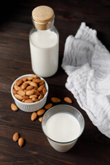 Almond milk in a glass and a glass bottle on dark wooden background.