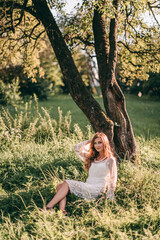 Portrait of a beautiful young blond woman in a white dress in a boho style walks in the park in summer at sunset.