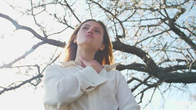 Young Attractive Woman Against The Background Of A Blurry Almond Tree And Blue Sky View From Below Slow Motion Shooting