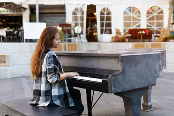 Teenage Girl in a plain shirt with long hair plays music on the piano outdoors on Haifa street,...