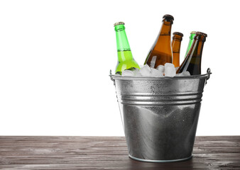 Metal bucket with bottles of beer and ice cubes on wooden table against white background. Space for text