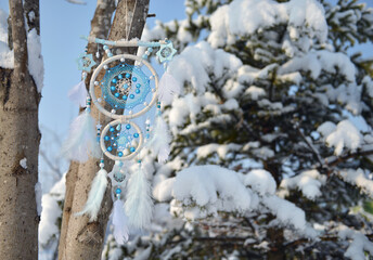 White and blue dreamcatcher hanging on tree against conifer covered with snow. Mystic wintertime...